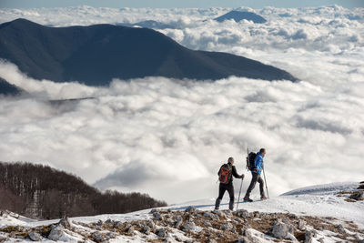 Full length of men walking on snow covered land against cloudscape