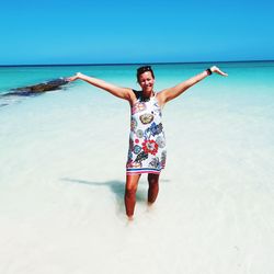 Portrait of woman with arms raised standing in sea against sky