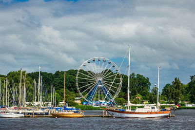 Sailboats moored on river against ferris wheel