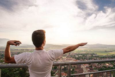 Rear view of man gesturing while standing by railing against sky