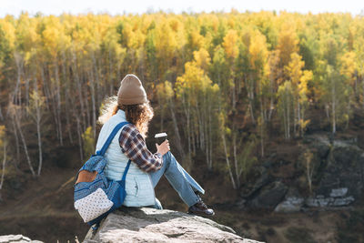 Young beautiful woman with curly hair in plaid shirt, jeans looks at the magic view of mountains 