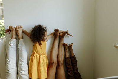 Girl with arms outstretched on parent's and brother's leg in front of wall