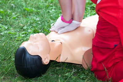 Midsection of paramedic practicing on cpr dummy at grassy field