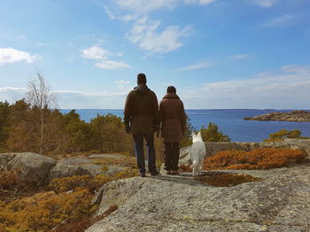 Rear view of men standing on rock by sea against sky