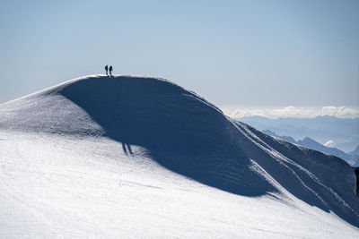 Two mountaineers stand silhouetted atop the ridge of a glacier on mt. baker