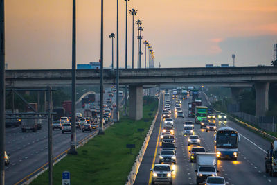 Traffic on bridge in city against sky during sunset