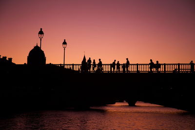 Silhouette of people on bridge over river during sunset