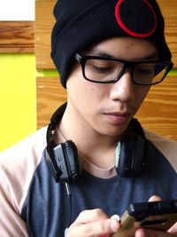 Close-up of young man with headphones wearing knit hat using mobile phone