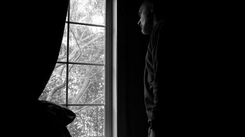 Rear view of man looking through window at home