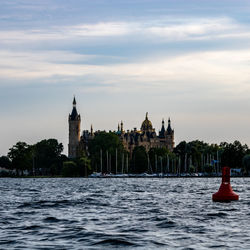 Buildings at waterfront against cloudy sky