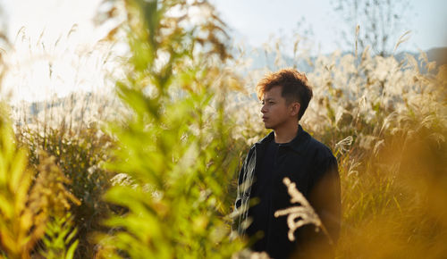 Young man looking away while standing on field