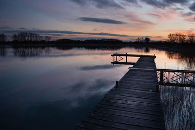 Wooden jetty on a quiet lake, evening colored clouds by sunset