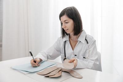 Doctor holding insoles while writing on paper