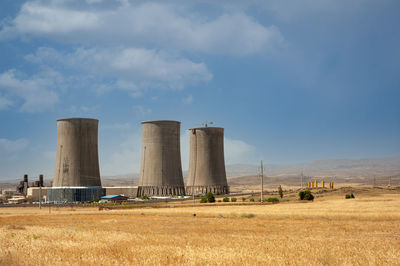 Nuclear power plant cooling towers, big chimneys beside wheat field with partly cloudy sky