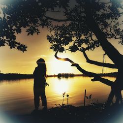 Silhouette man fishing by lake against sky during sunset