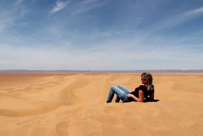 Woman relaxing on sand at desert against sky