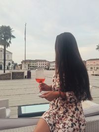 Young woman drinking water from glass against sky