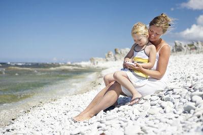 Mother with daughter sitting on rocky beach