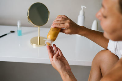 Close-up of a gold-colored moisturizer in the hands of a woman woman. pouring lotion into hand