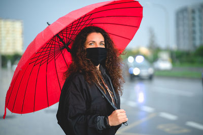Portrait of a woman with a mask and a red umbrella looking at camera