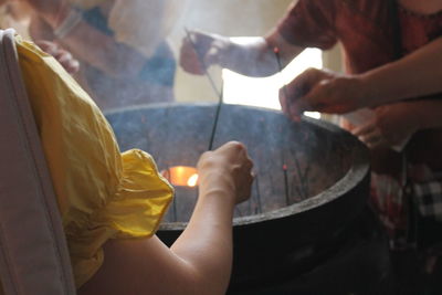 Midsection of people keeping incenses in container