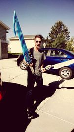 Portrait of happy young man standing by car on sunny day