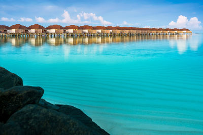Scenic view of water villas in maldives with turquoise pristine water and dramatic sky