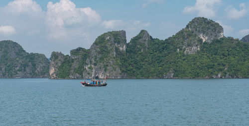 Boat sailing on sea by mountains against sky