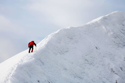 Low angle view of mountaineer climbing snowcapped mountain against sky