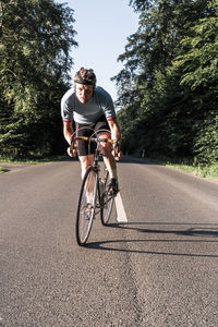 Portrait of young man riding bicycle on road during sunny day