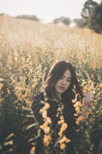 Thoughtful young man standing amidst yellow flowers on field