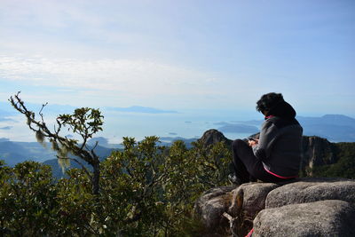 Side view of woman sitting on mountain against sky