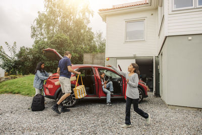 Girl playing with ball near family loading stuff in electric car by house