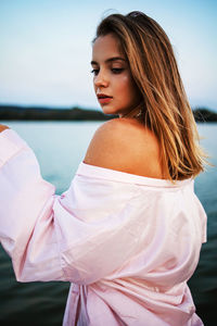 A beautiful blonde girl in a pink bathrobe stands near lake at sunset. fairy story.