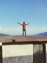 Rear view of man standing on rooftop against sky