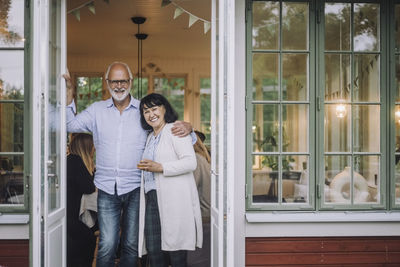 Portrait of happy senior man with arm around woman standing at doorway