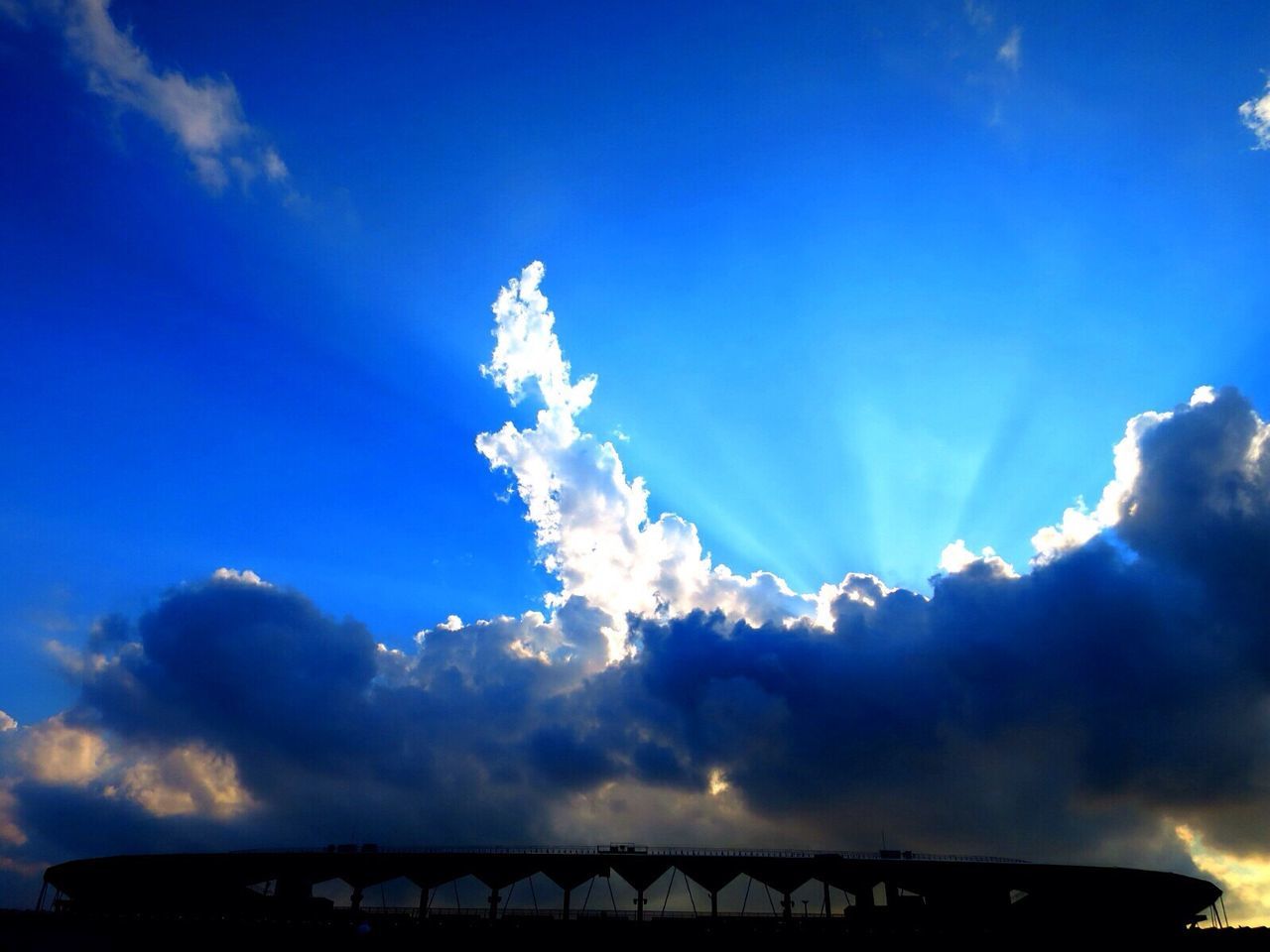 sky, blue, cloud - sky, low angle view, cloud, beauty in nature, cloudy, silhouette, nature, scenics, built structure, sunlight, cloudscape, tranquility, sunbeam, tranquil scene, outdoors, building exterior, high section, architecture