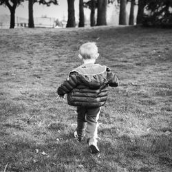 Rear view of boy walking on grassy field