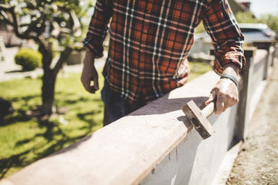 Midsection of senior man checking surrounding wall at yard