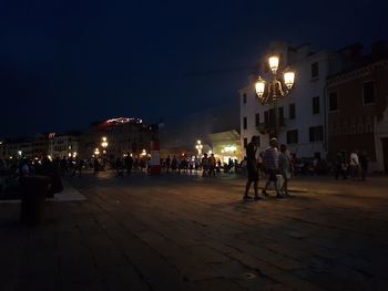 People on street against illuminated buildings in city at night