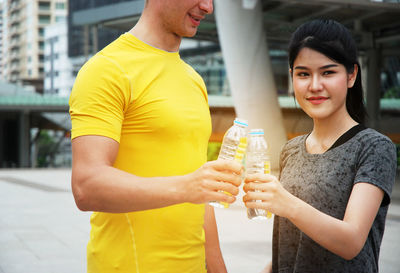 Smiling young woman holding drink while standing in city