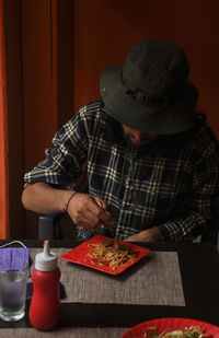 A bearded and long haired young man eating noodles in the restaurant during covid-19 pandemic.