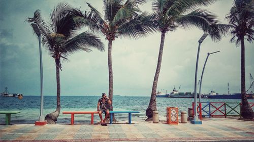 Full length of young man sitting on bench against sky