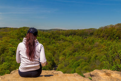 Full length of young woman sitting on landscape against sky