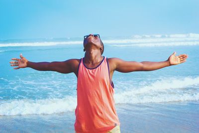 Happy man standing with arms outstretched at beach against sky