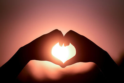 Silhouette hand holding heart shape against sky during sunset