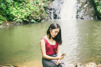 Young woman using mobile phone while standing by lake