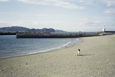 Woman sitting at beach against sky