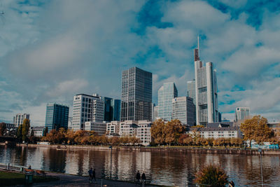 Modern buildings by river against sky in city