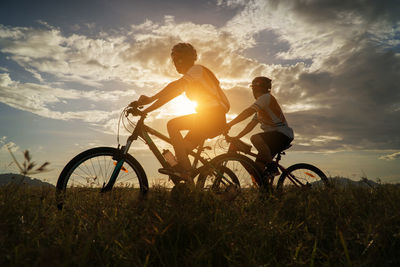 Men with bicycle on field against sky during sunset